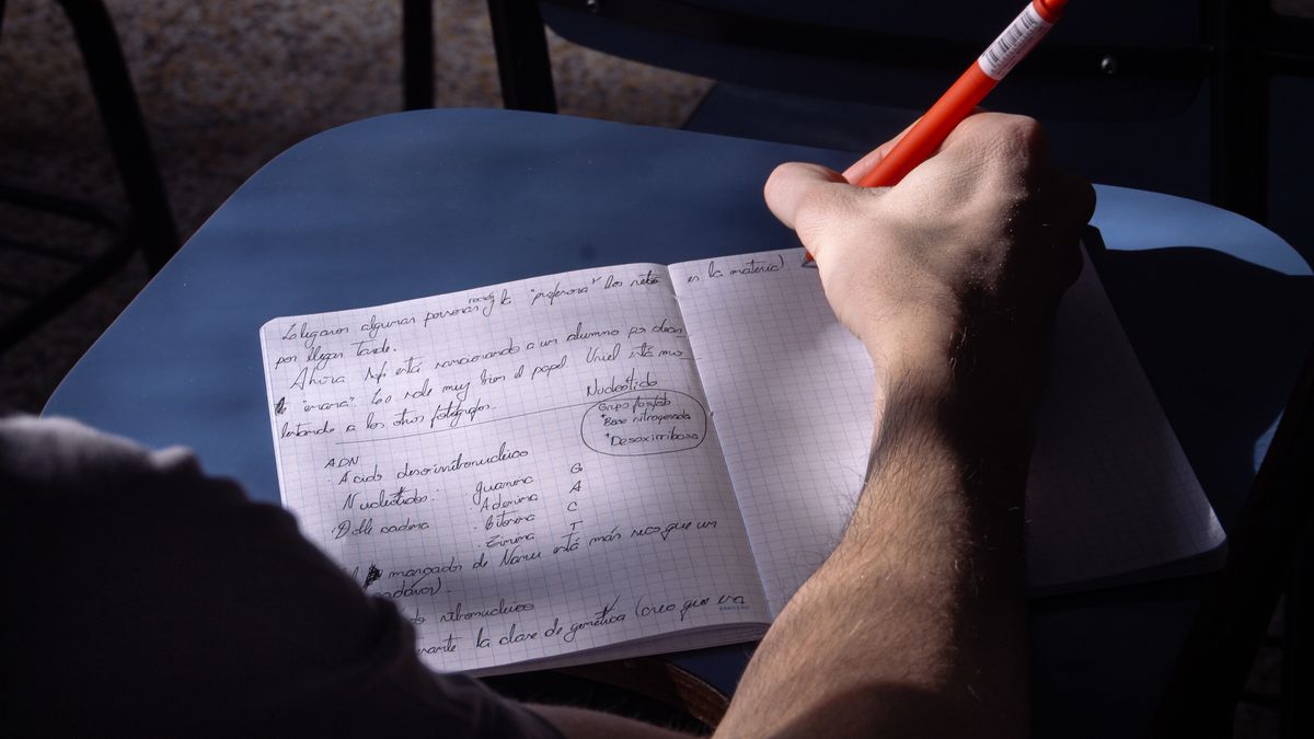 机でノートに英語を書いて勉強している人