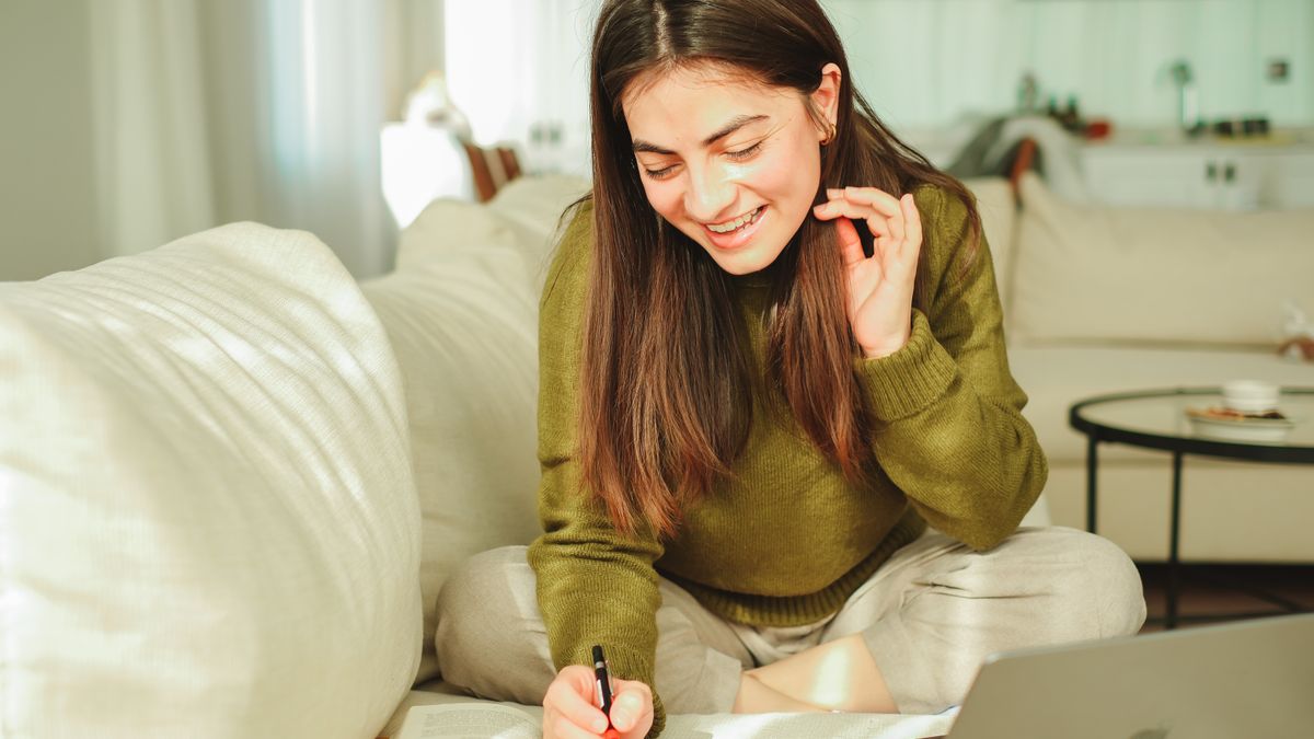 自宅でノートパソコンとノートを使って笑顔で勉強する女性