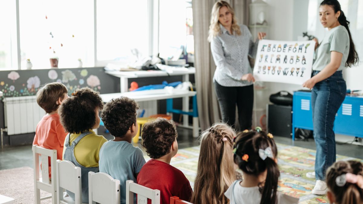 nursery teacher reading picture book to children in classroom