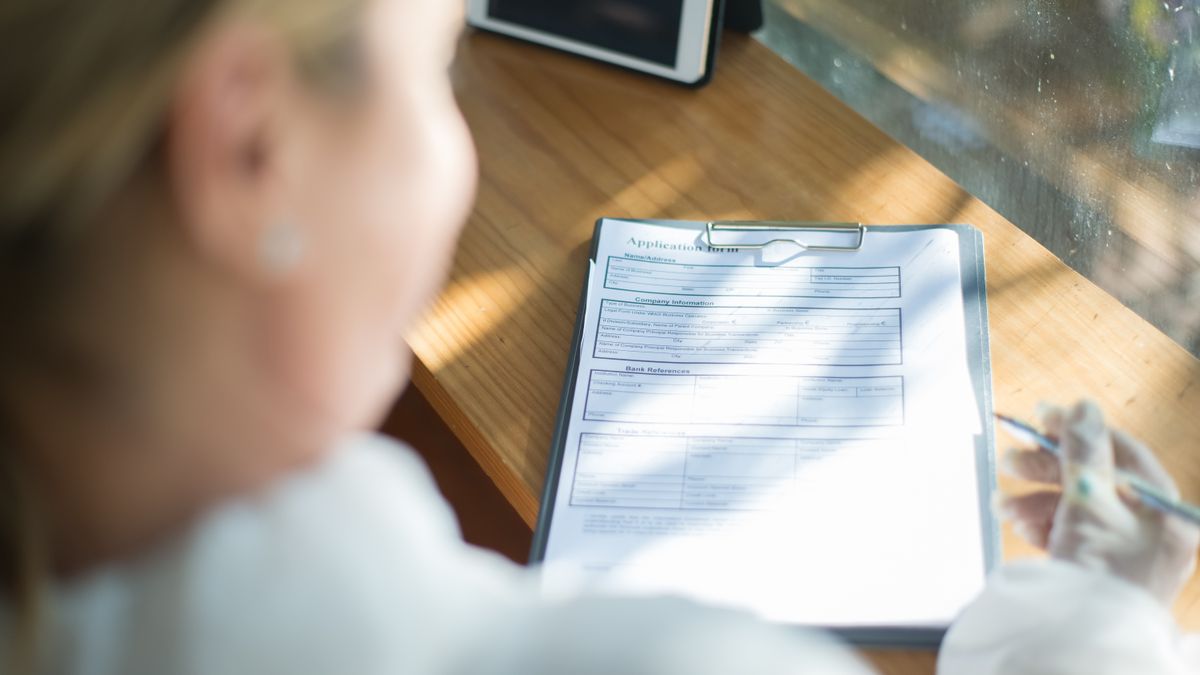 person filling out application form documents with pen at desk