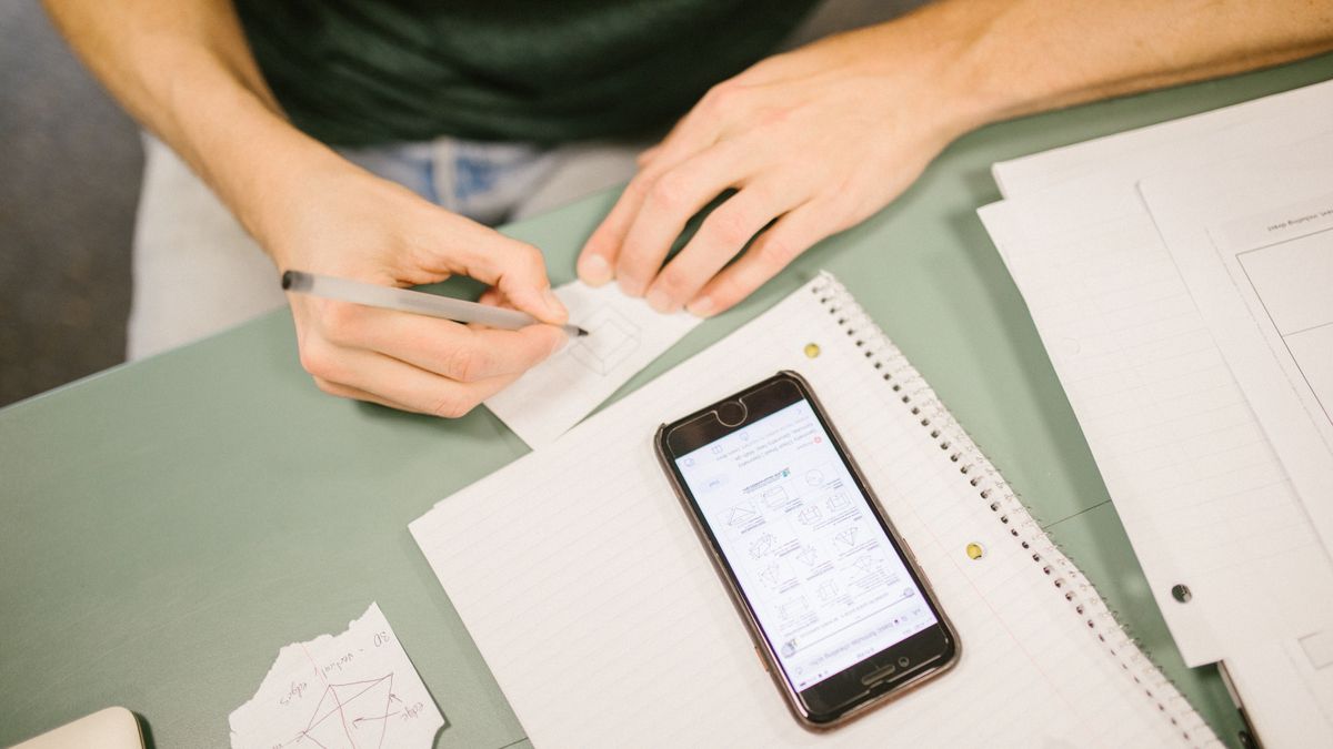 ノートとスマートフォンを使ってデスクで勉強する人