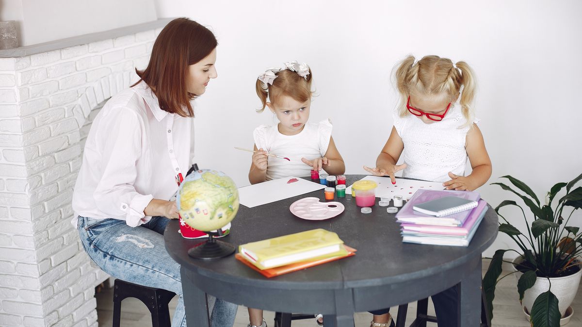 mother studying at table while children play nearby