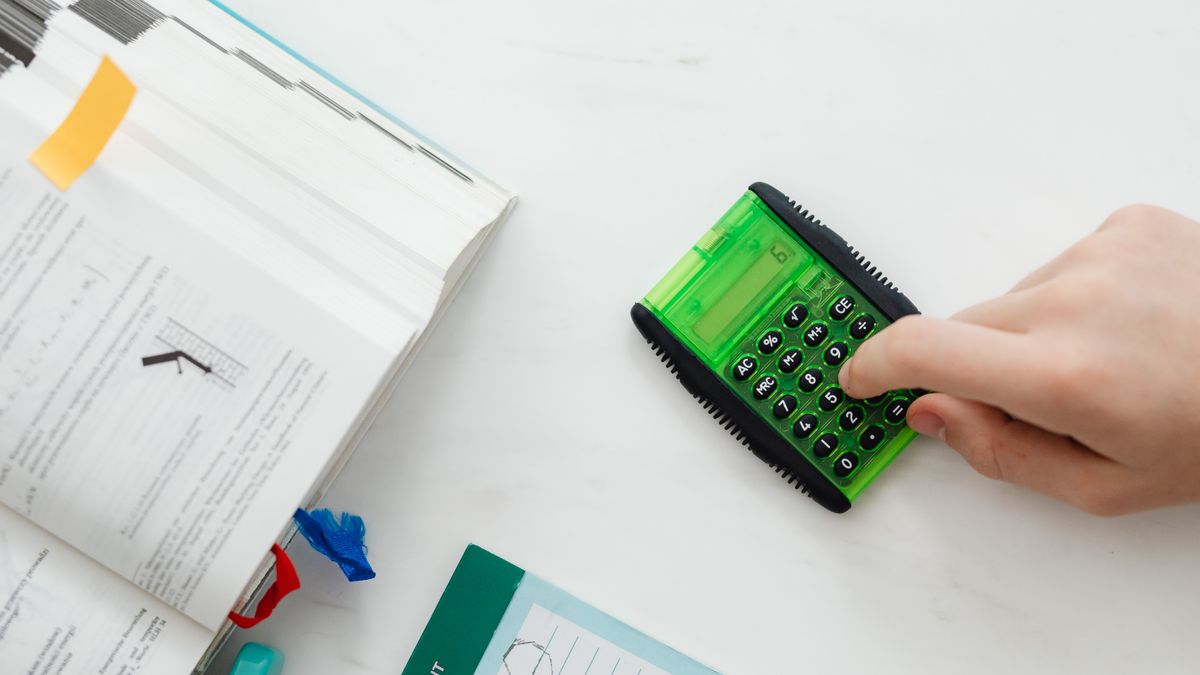 person solving calculation problems with textbook calculator at desk