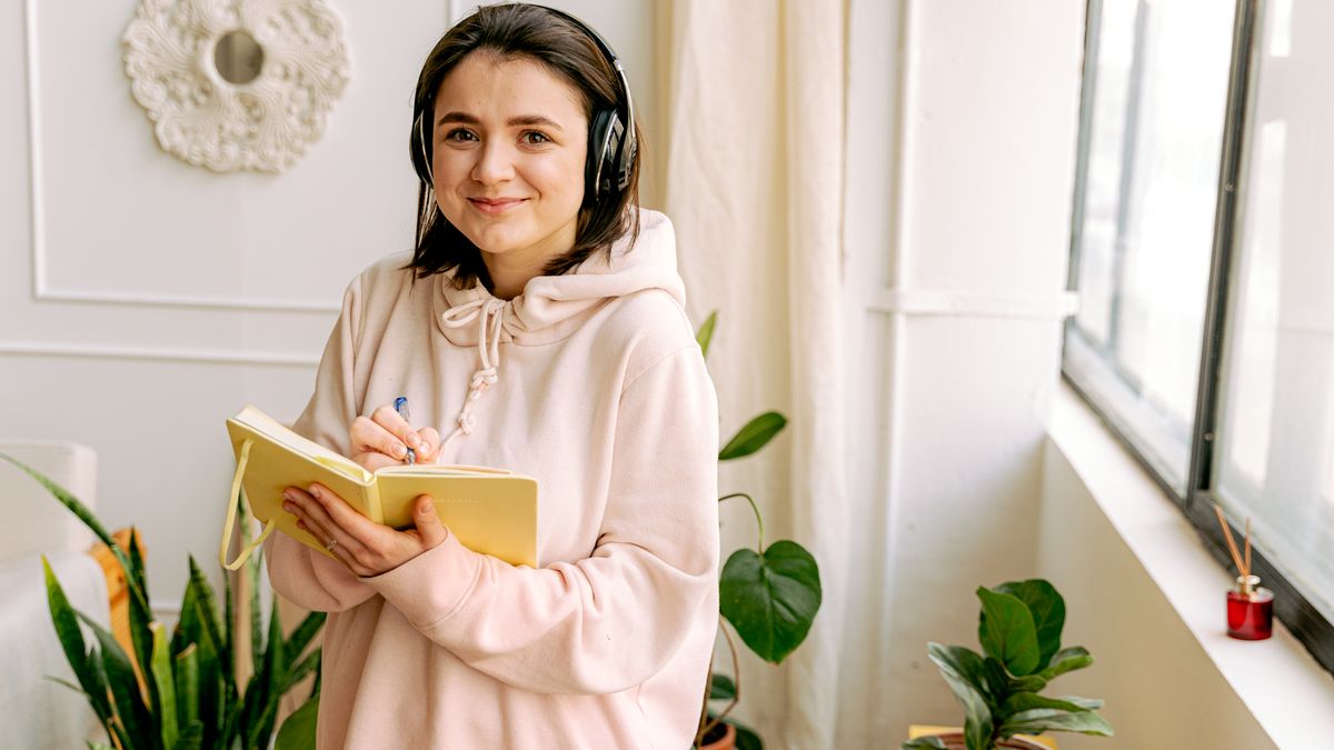 person taking notes while listening with headphones