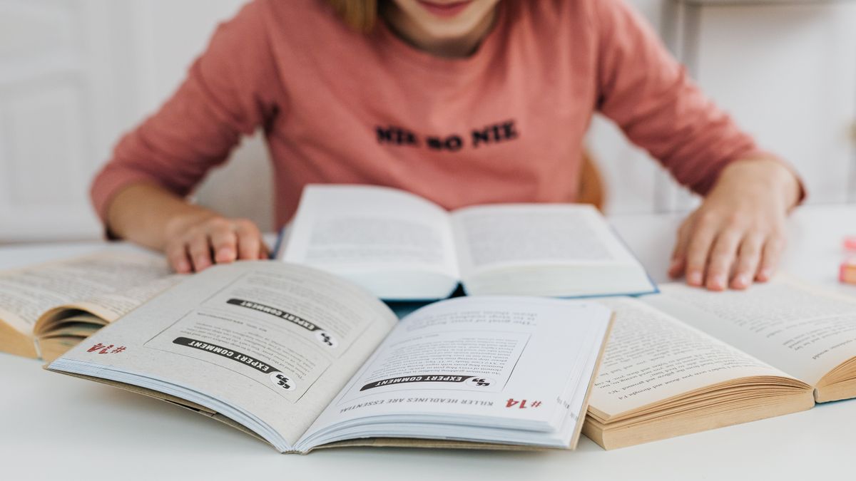 student surrounded by multiple thick textbooks studying